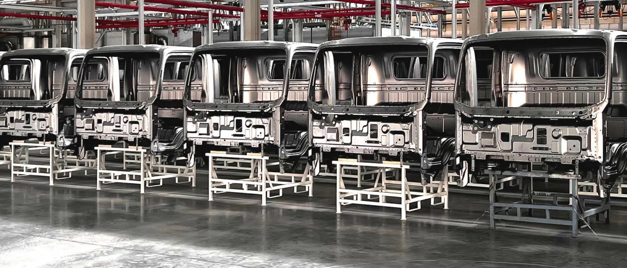 Rows of unpainted truck cab bodies standing in sequence on the floor of a production hall.