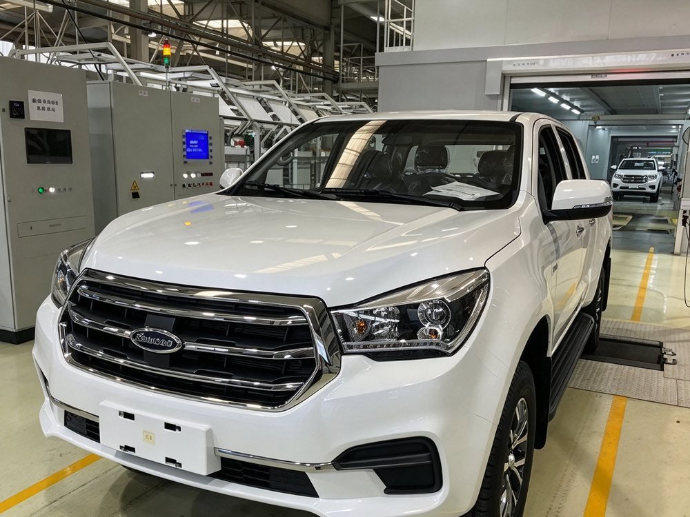 A white double-cab pickup on an assembly line inside a vehicle plant, its body fully assembled.