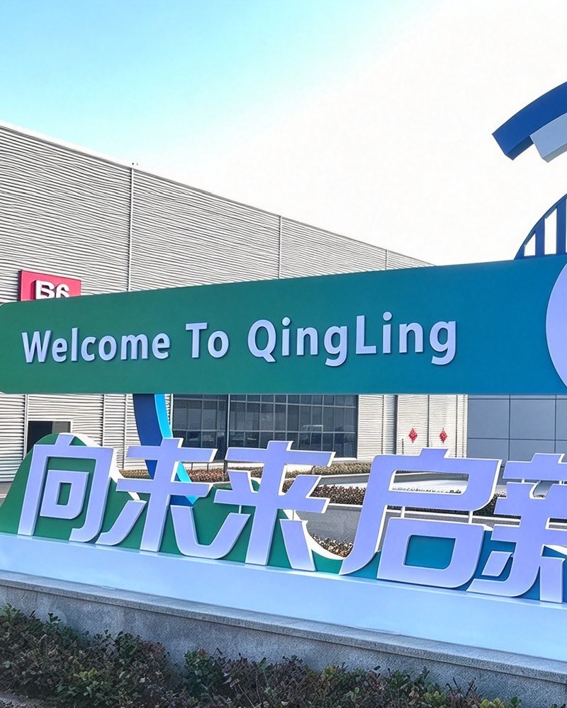 A large plant entrance sign reading "Welcome To QingLing", with a warehouse building behind it.